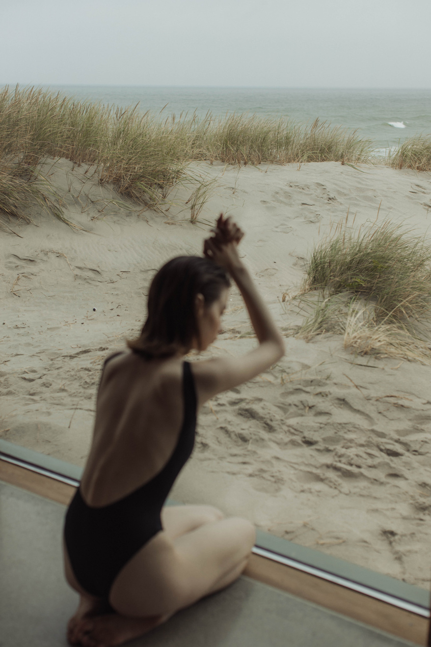 A Woman in Black Swimwear Sitting on the Floor Near the Glass Wall